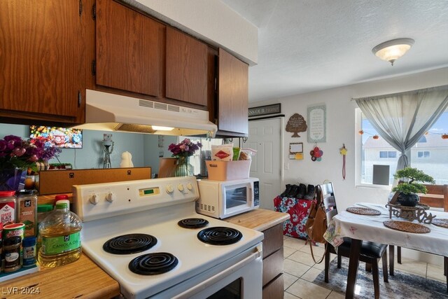 4740 Corsaire Ave, Las Vegas, NV 89115 - kitchen featuring white appliances, under cabinet range hood, light countertops, light tile patterned flooring, and brown cabinets