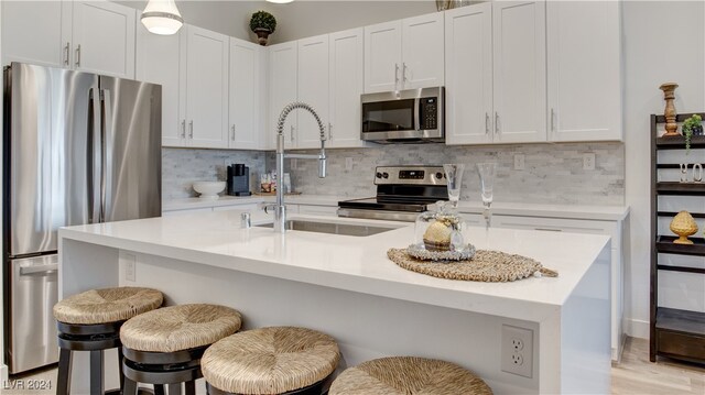 kitchen with a center island with sink, sink, white cabinetry, appliances with stainless steel finishes, and a breakfast bar area