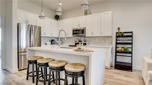 kitchen with a breakfast bar, stainless steel appliances, a kitchen island with sink, and light hardwood / wood-style flooring