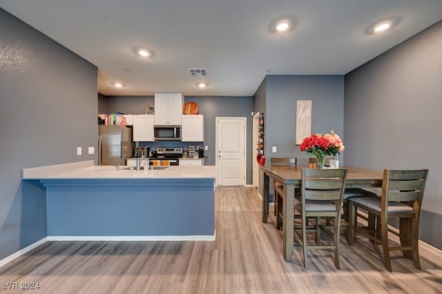 kitchen with sink, light hardwood / wood-style flooring, kitchen peninsula, white cabinets, and appliances with stainless steel finishes