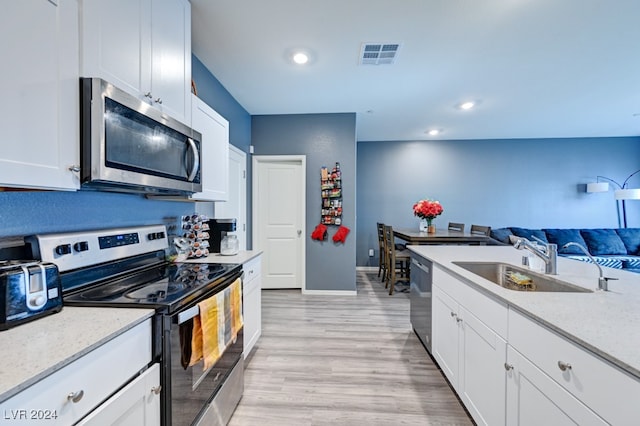 kitchen with sink, light stone counters, appliances with stainless steel finishes, white cabinets, and light wood-type flooring