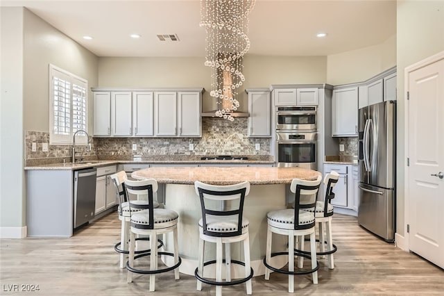 kitchen with light stone countertops, stainless steel appliances, sink, light hardwood / wood-style floors, and a kitchen island