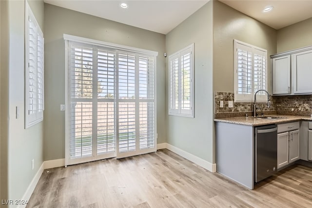 kitchen with light stone countertops, dishwasher, sink, light hardwood / wood-style flooring, and backsplash