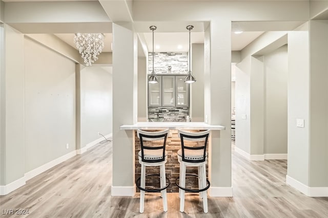 kitchen with hanging light fixtures, light hardwood / wood-style flooring, decorative backsplash, kitchen peninsula, and a chandelier