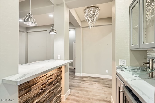 kitchen with light stone countertops, sink, light hardwood / wood-style flooring, a notable chandelier, and hanging light fixtures