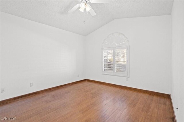 empty room with a textured ceiling, wood finished floors, a ceiling fan, baseboards, and vaulted ceiling