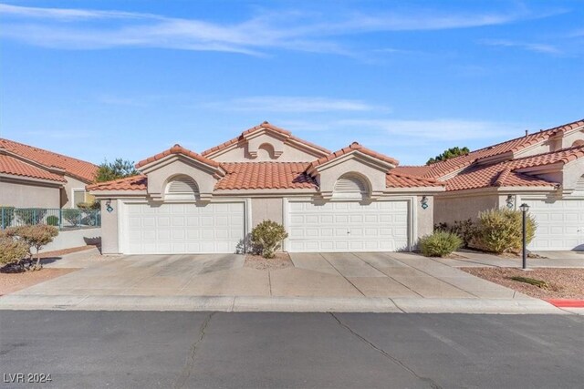 mediterranean / spanish home with a garage, a tile roof, driveway, and stucco siding