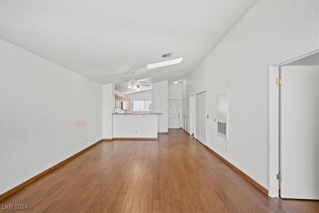 unfurnished living room with visible vents, lofted ceiling with skylight, a ceiling fan, wood finished floors, and baseboards