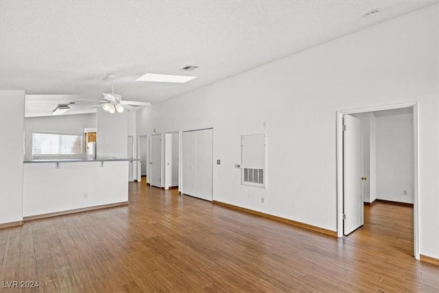 unfurnished living room with vaulted ceiling with skylight, visible vents, a ceiling fan, wood finished floors, and a textured ceiling