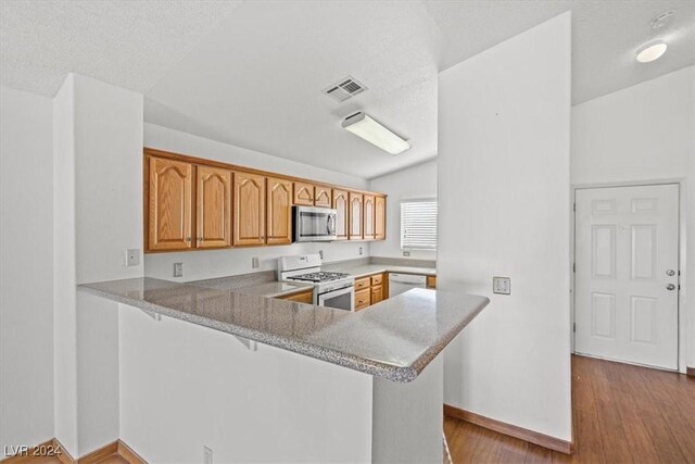 kitchen with a peninsula, white appliances, visible vents, a kitchen bar, and dark wood finished floors