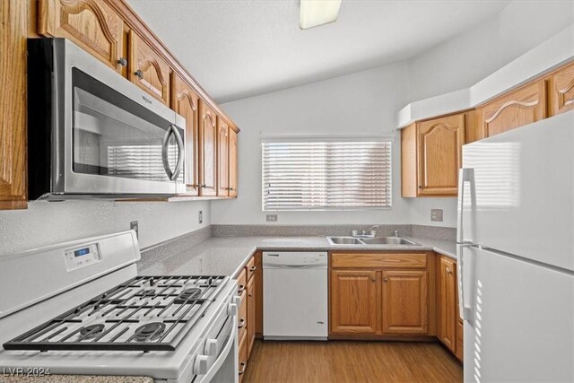 kitchen with white appliances, a sink, vaulted ceiling, light countertops, and light wood finished floors