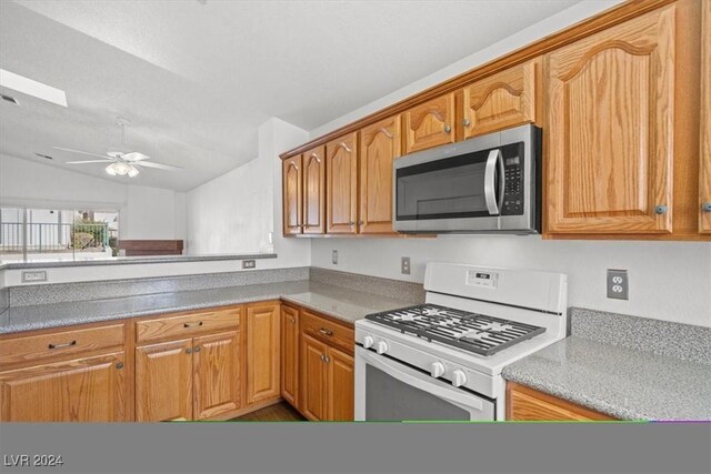 kitchen with ceiling fan, white range with gas stovetop, vaulted ceiling, brown cabinetry, and stainless steel microwave