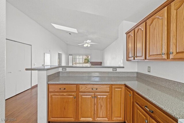 kitchen featuring brown cabinets, ceiling fan, wood finished floors, vaulted ceiling with skylight, and a peninsula