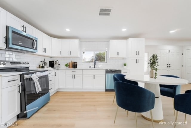 kitchen with decorative backsplash, appliances with stainless steel finishes, light wood-type flooring, and white cabinetry