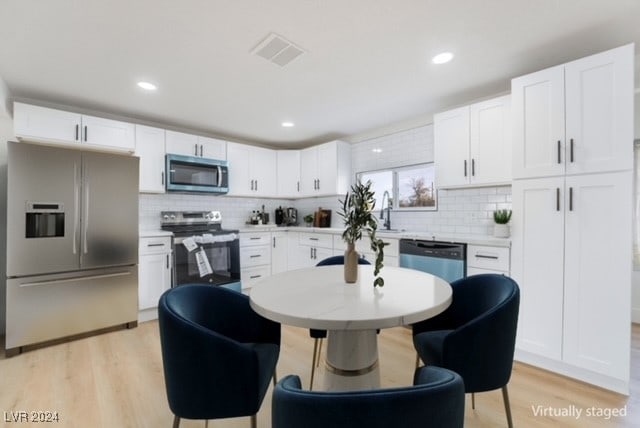 kitchen featuring appliances with stainless steel finishes, backsplash, sink, light hardwood / wood-style flooring, and white cabinetry