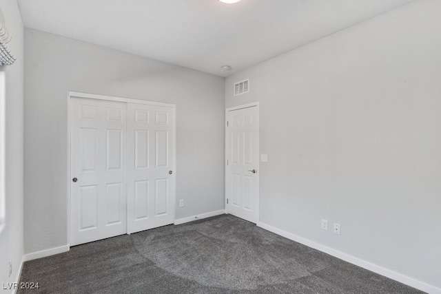 unfurnished bedroom with dark carpet and a closet