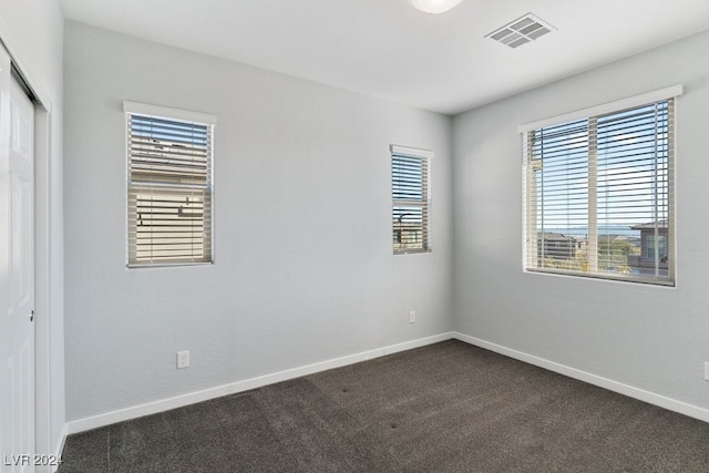 spare room featuring dark colored carpet and plenty of natural light