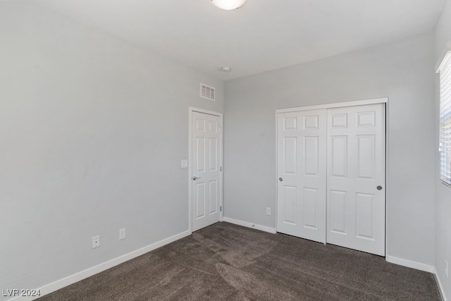 unfurnished bedroom with dark carpet and a closet