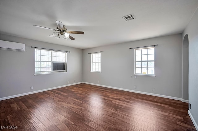 unfurnished room featuring a wealth of natural light, dark hardwood / wood-style flooring, a wall mounted AC, and ceiling fan