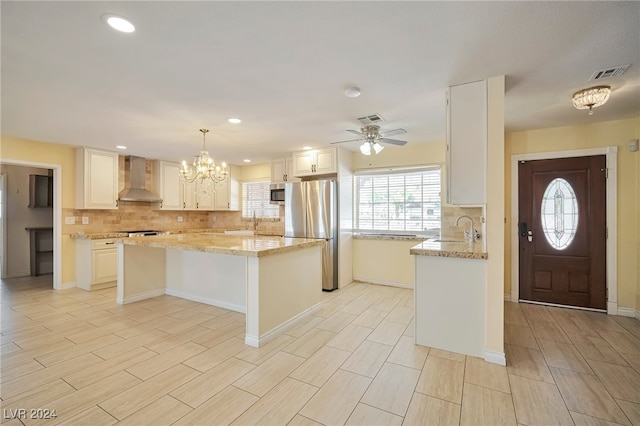 kitchen with pendant lighting, a center island, wall chimney exhaust hood, white cabinetry, and stainless steel appliances