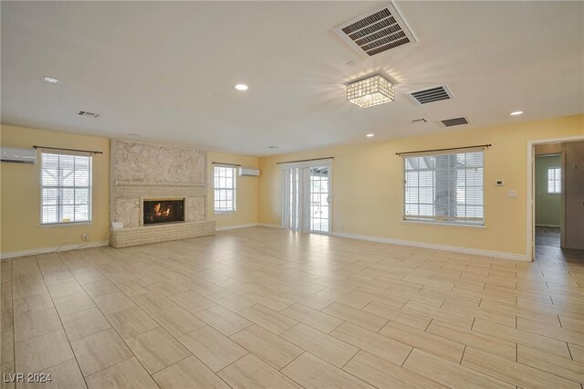 unfurnished living room featuring a wall mounted AC, a wealth of natural light, and a fireplace