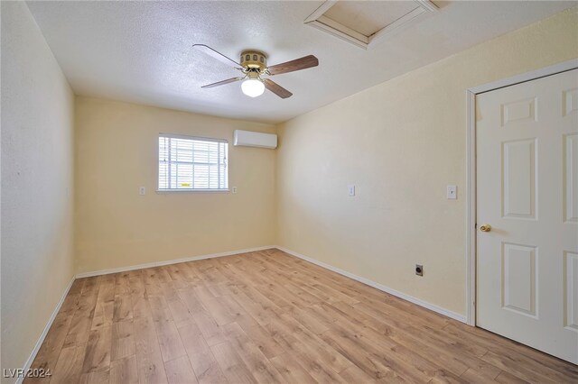 unfurnished room with ceiling fan, light wood-type flooring, an AC wall unit, and a textured ceiling