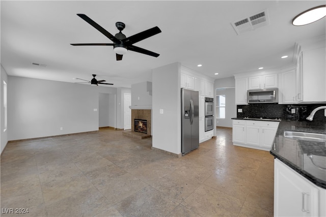 kitchen featuring stainless steel appliances, ceiling fan, sink, dark stone countertops, and white cabinetry