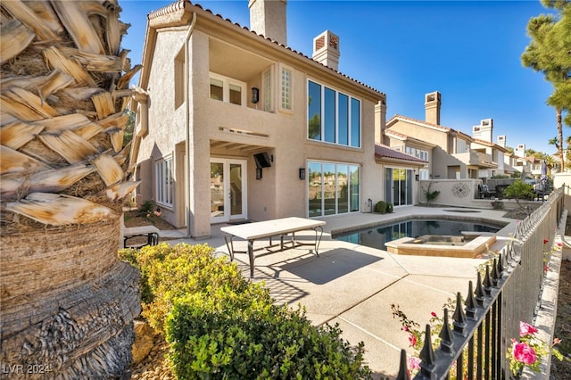 rear view of property with a swimming pool with hot tub and a patio area