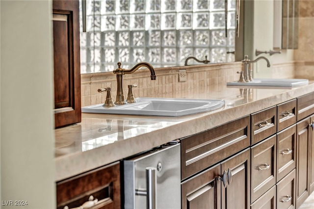 interior space featuring backsplash, wine cooler, light stone counters, and sink