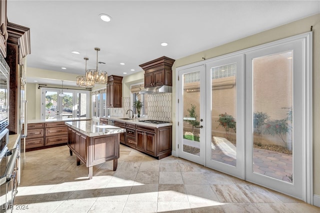 kitchen featuring sink, stainless steel gas cooktop, tasteful backsplash, decorative light fixtures, and a kitchen island