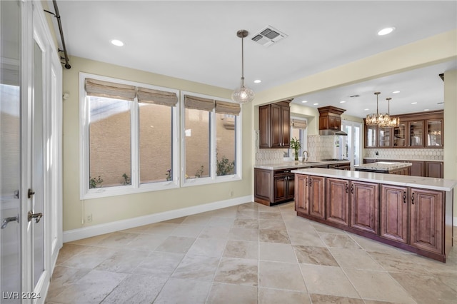 kitchen featuring tasteful backsplash, sink, hanging light fixtures, and a center island with sink