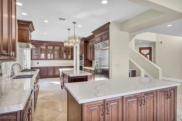 kitchen featuring pendant lighting, backsplash, stainless steel built in fridge, light stone countertops, and a kitchen island