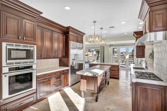 kitchen with tasteful backsplash, a notable chandelier, built in appliances, decorative light fixtures, and a kitchen island