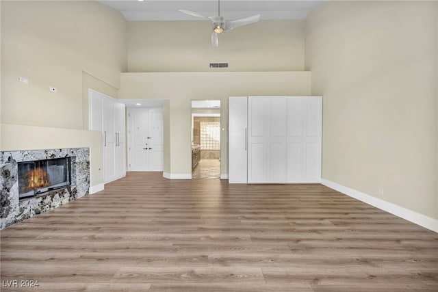 living room with ceiling fan, a fireplace, a high ceiling, and light wood-type flooring