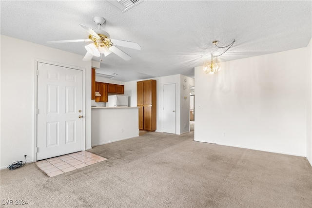 unfurnished living room with a textured ceiling, ceiling fan with notable chandelier, and light colored carpet