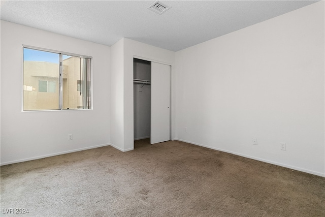 unfurnished bedroom with a textured ceiling, carpet floors, and a closet