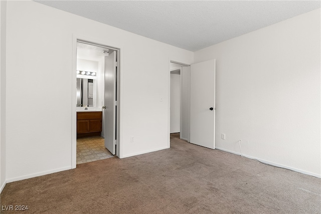 unfurnished bedroom with light colored carpet, a textured ceiling, and ensuite bath