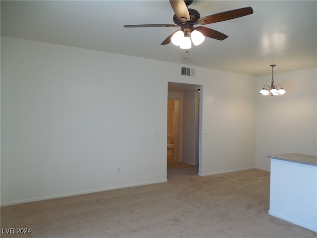 empty room featuring ceiling fan with notable chandelier and light colored carpet