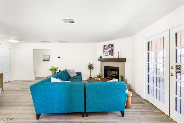 living room with a tile fireplace, french doors, and light wood-type flooring