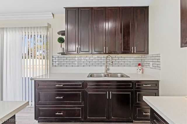 kitchen featuring sink, light hardwood / wood-style flooring, decorative backsplash, dark brown cabinets, and ornamental molding