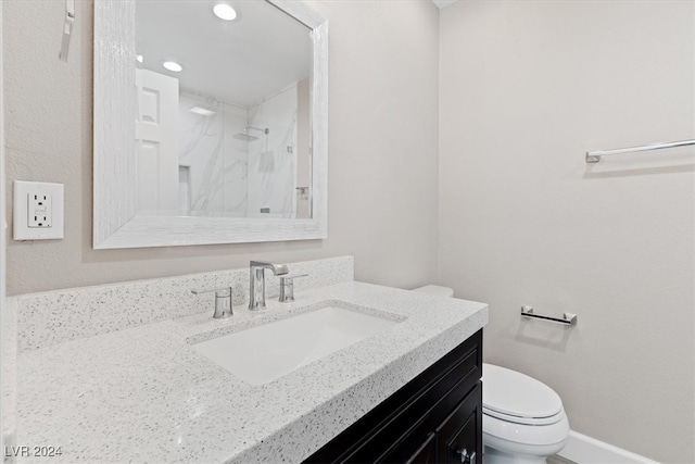 bathroom featuring a tile shower, vanity, and toilet