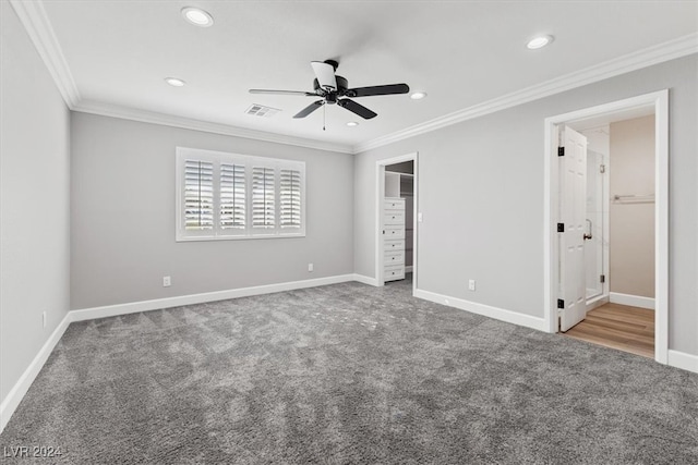 unfurnished bedroom featuring carpet, a walk in closet, crown molding, and ceiling fan