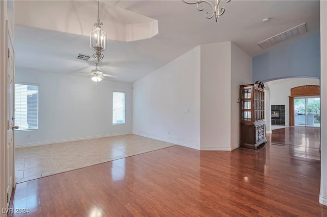 unfurnished room featuring a tile fireplace, hardwood / wood-style floors, and ceiling fan with notable chandelier