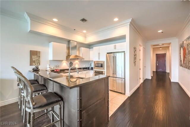 4525 Dean Martin Dr Unit 302, Las Vegas, NV 89103 - kitchen with stainless steel appliances, wall chimney exhaust hood, dark countertops, a peninsula, and white cabinetry