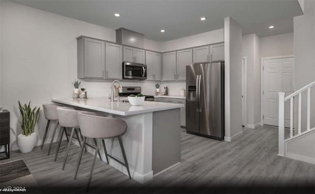 kitchen with gray cabinetry, a breakfast bar area, stainless steel appliances, and kitchen peninsula