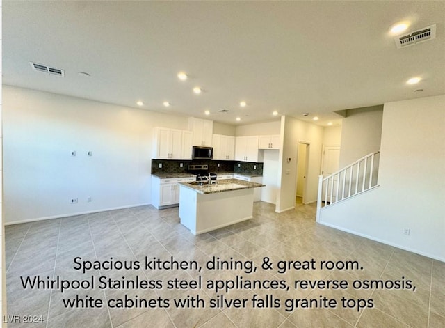 kitchen featuring sink, dark stone countertops, tasteful backsplash, an island with sink, and white cabinets