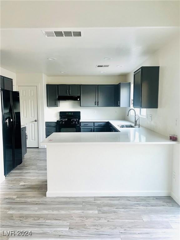 kitchen with black appliances, kitchen peninsula, sink, and light hardwood / wood-style flooring