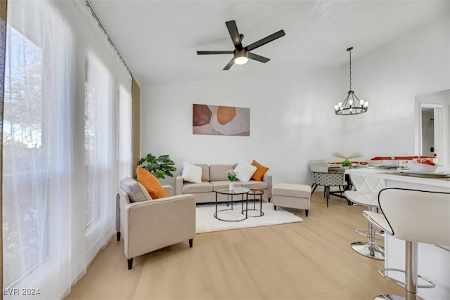 living room with plenty of natural light, lofted ceiling, ceiling fan with notable chandelier, and light hardwood / wood-style flooring