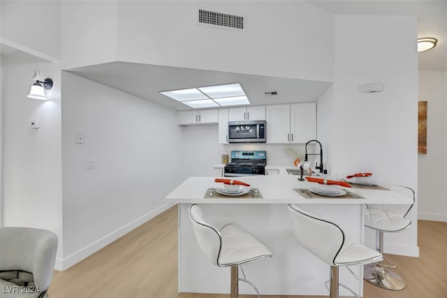 kitchen with kitchen peninsula, black gas range oven, light hardwood / wood-style floors, a kitchen bar, and white cabinetry