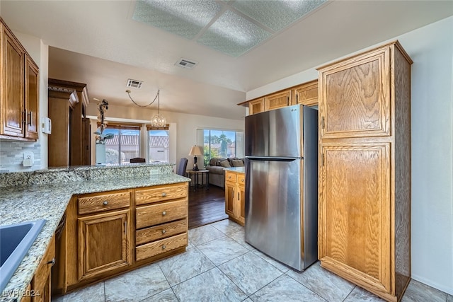 kitchen with light stone countertops, stainless steel fridge, tasteful backsplash, a notable chandelier, and light hardwood / wood-style floors